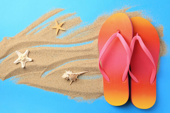 Flip flops and sand on light blue background, flat lay. Beach accessories