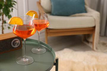 Tasty cocktail in glasses with orange slices and radio set on table in room, space for text. Relax at home