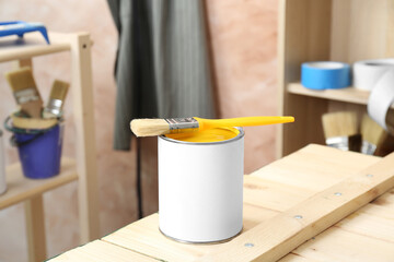 Can of yellow paint with brush on wooden table indoors - obrazy, fototapety, plakaty