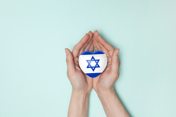Heart with print of Israel flag in female hands. Flat lay. Copy space. - obrazy, fototapety, plakaty
