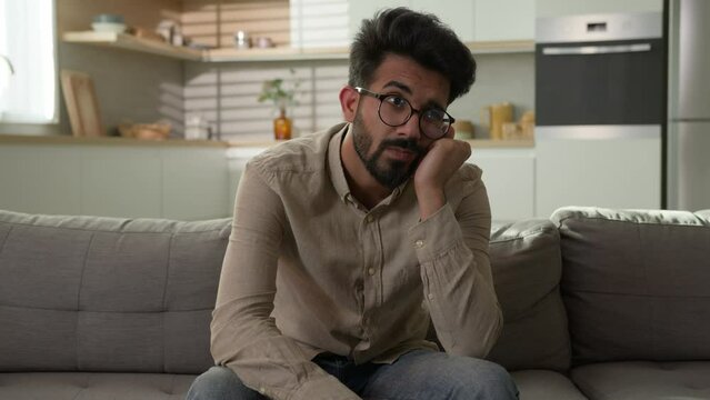 Pensive Indian Arabian man bored on home couch thinking deep in thoughts difficult decision tired exhausted thoughtful worried male boring weekend feel headache problem solution depression melancholy