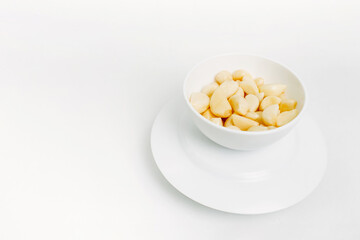 Peeled garlic cloves in a white plate on a white background.