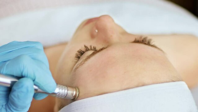 Beautician cosmetologist makes a procedure Microdermabrasion peeling of the face skin. Hardware cosmetology in clinic salon for client. Diamond face clean.
