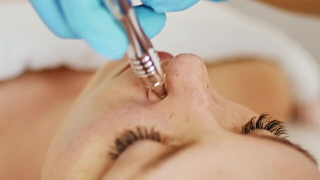 Beautician cosmetologist makes a procedure Microdermabrasion peeling of the face skin. Hardware cosmetology in clinic salon for client. Diamond face clean.