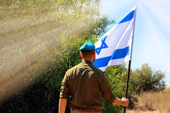 Israeli soldier stands in a field with Flag of Israel in the spectrum of sunlight. Concept this photo - Jewish patriot, IDF, Memorial Day for the Fallen Soldiers of the Wars, Israel Independence Day