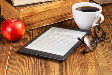 E-book, cup of coffee, apple and glasses next to a stack of vintage books in the library. Education concept.