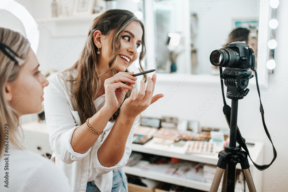 Wall mural Happy young woman streaming a beauty makeup vlog from home or workshop. Beautiful online content creator cosmetician applying makeup and explaining some work tools. Vlogging and online channel work.