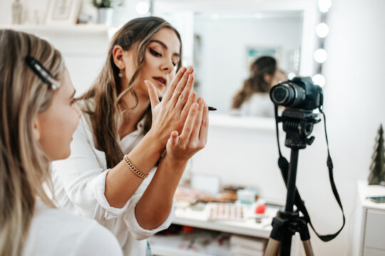 Happy young woman streaming a beauty makeup vlog from home or workshop. Beautiful online content creator cosmetician applying makeup and explaining some work tools. Vlogging and online channel work.