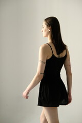 Fototapeta premium Portrait of a brunette girl without make up on a grey backgroung in a black summer clothes. Back view