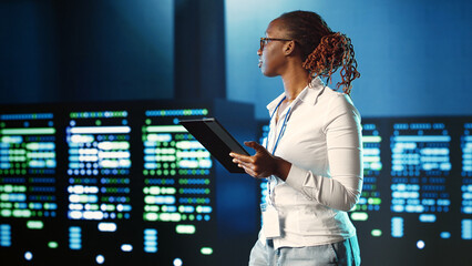 African american specialist strolling through server rows providing processing resources for different workloads. Experienced woman monitoring supercomputers tasked with solving complex operations