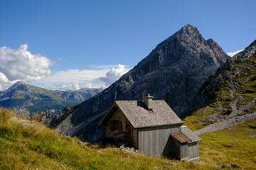 Fototapeta na wymiar Hangkante auf Hochebene mit Bergspitze im Hintergrund und naher Hütte im Vordergrund