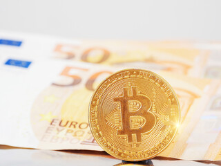 Gold shiny bitcoin with flare, Euro banknotes out of focus in in the background. Economy and financial background. Grey color background. Vertical image. Popular cryptocurrency or payment system.