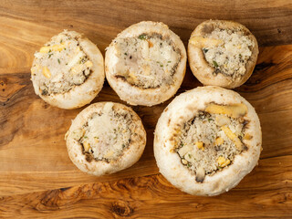 Stuffed mushrooms cups on a wooden board and table. High quality product with breadcrumbs, cheese and herbs ready for oven cooking.