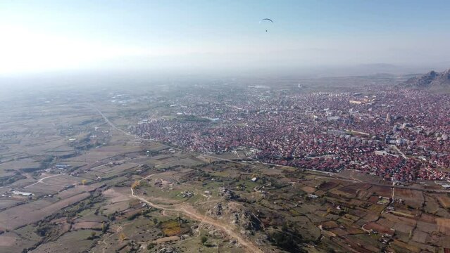 Person paragliding over eastern european town. Aerial drone video of Prilep in North Macedonia.