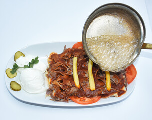 Iskender kebab pictured pouring butter on it, accompanied by vegetables, yoghurt and french fries. Turkish doner kebab