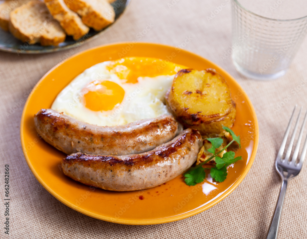 Poster Fried sausages, potato and sunny-side up eggs dished up in a plate on the laid restaurant table - Posters
