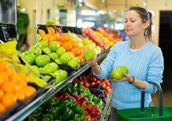 Positive middle-aged woman purchaser holding fresh apples at the counter in grocery store