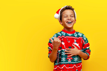 funny african american boy in christmas clothes pointing and advertising empty space and joking and...