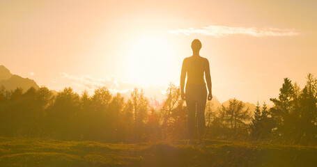 SILHOUETTE, LENS FLARE: Athletic lady standing on mountaintop at golden sunset