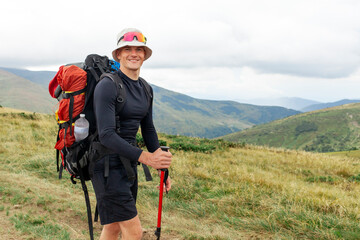 male tourist with backpack and hiking equipment stands in the mountains against the backdrop of...