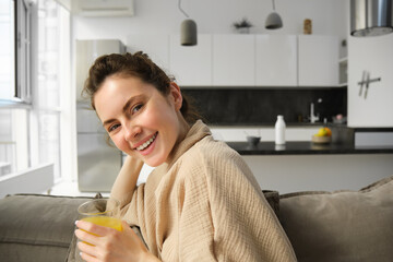 Women wellbeing and lifestyle. Beautiful young woman on sofa, drinking orange juice, relaxing at...
