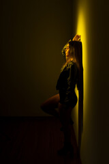 A young model woman leaning against a yellow -illuminated wall.