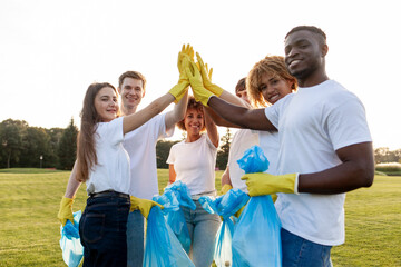 team of volunteers in gloves and with garbage bags rejoice together at success and high five