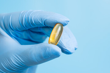 Doctor, pharmacist or scientist hand in blue glove holding omega 3 capsule. Vitamin pill or...