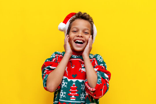 African American Boy In Christmas Clothes Smiling On Yellow Background, Happy 9 Year Old Child In Santa Hat Laughing