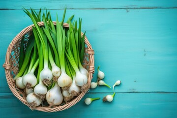 Fresh onion bulbs leeks and garlic in a wicker basket on a light blue wooden table photographed from above