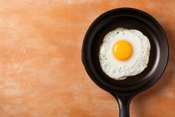 Overhead view of fried egg in frying pan on yellow backdrop