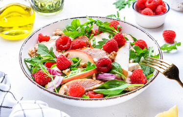 Fresh salad with raspberries, grilled chicken, pears, cheese, onion, walnuts, spinach and arugula, white table background, top view