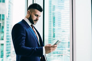 Thoughtful adult executive man using smartphone in office