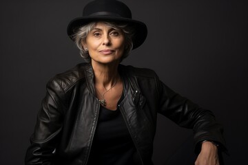 Elegant mature woman in hat and leather jacket posing on dark background