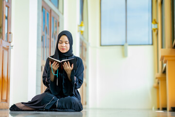 The image of an Asian Muslim woman in the Islamic religion in hijab in black  color. reading the...