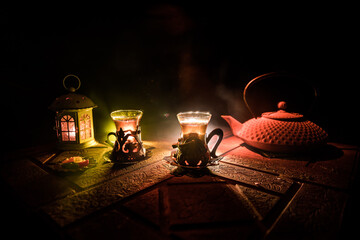 Arabian tea in glass with eastern snacks on a carpet on dark background with lights and smoke. Eastern tea concept. Empty space. Selective focus.