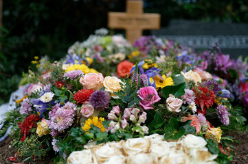 funeral wreath on a grave with white ribbons and colorful flowers with a wooden cross in a blurred background
