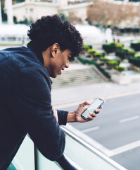 Cheerful African American man using smartphone outdoors while leaning on railing