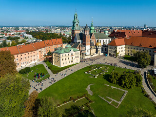 Royal Wawel Gothic Cathedral in Krakow, Poland, with Renaissance Sigismund Chapel with golden dome, walking people, and lawn with foundations of old destroyed buildings and two churches. Aerial view