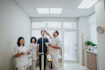 Three doctors measuring young patient height using metric scale at the hospital.