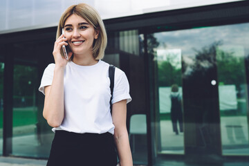 Pleased young modern woman having phone call on street