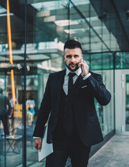 Serious manager speaking on smartphone outside business center