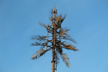 Internet transmitter mast with artificial tree camouflage against a blue sky background on a sunny...