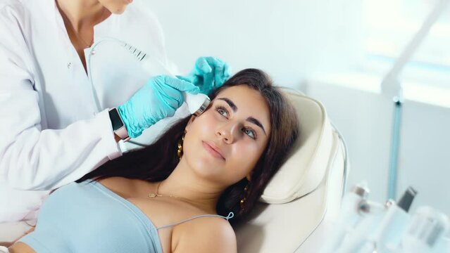 Young female patient receiving facial procedure with high frequency ultrasonic vibration attachment to enhance efficacy of skincare products and improving skin texture. Modern hardware cosmetology