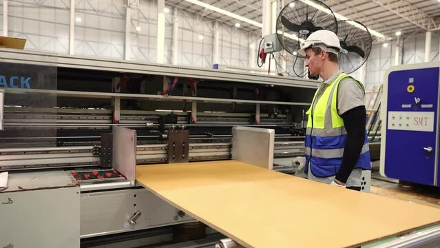 Male technician stands operate corrugated cardboard die-cutting machine. The machine is operating safely with safety equipment in the logistics cardboard production factory.
