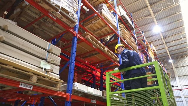 Team two male and female workers board forklift to inspect cardboard boxes on a pallet rack, secured by a team of safety drivers inside an export logistics manufacturing facility building.
