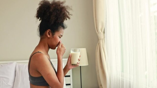 Pregnant young mother of Thai-African descent sits in her bedroom preparing to drink pasteurized milk but is so sick with the stench that she cannot drink it : Concept healthcare for pregnant women.