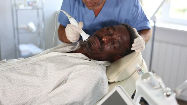 Adult African American undergoing high frequency ultrasound therapy to reduce fine wrinkles and rejuvenate facial skin by stimulating collagen production. Modern cosmetology and male grooming concept