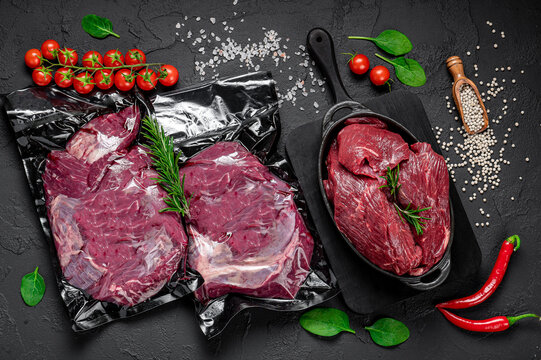 Raw organic marbled beef with spices on a wooden cutting board on a black slate, stone or concrete background.