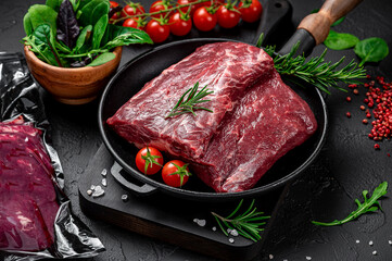 Raw organic marbled beef with spices on a wooden cutting board on a black slate, stone or concrete background.